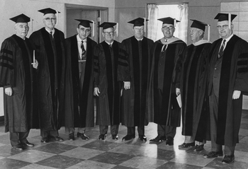 Egyetemi diplomaosztó csoportkép Férfiak egyetemi talárban és sapkában állnak egy szobában, diplomaosztó ünnepségen.