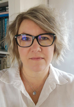 Fehér blúz és nyaklánc könyvespolc előtt Személy fehér blúzban, nyaklánccal, könyvespolc előtt, háttérben könyvek.