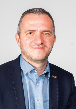 Férfi kék ingben és sötétkék zakóban Férfi kék inget és sötétkék zakót visel, a képen a felsőtest látható.