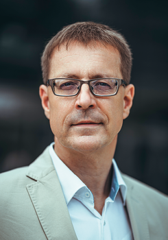 Férfi világos zakóban és fehér ingben Férfi világos zakót és fehér inget visel, háttér homályos.