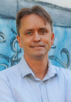 Férfi világoskék ingben graffiti háttér előtt Férfi világoskék ingben áll, háttérben graffiti látható.