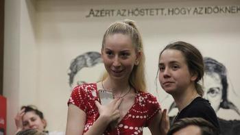 Fiatal nő piros ruhában okostelefonnal, háttérben felirat és rajz