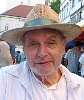Kalapos személy városi háttérrel Kalapot viselő személy fehér ingben, városi környezetben emberek és épületek háttérben.