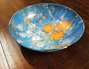 Kintsugi technikával javított kék virágmintás kerámia tál Kék alapon virágmintás kerámia tál, kintsugi technikával javítva, fa asztalon.