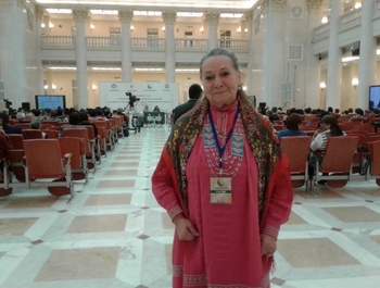 Konferencia résztvevője egy impozáns épületben Konferencia résztvevője áll a kamera előtt, háttérben a színpad és a közönség egy impozáns épületben.