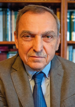Könyvespolc előtt álló öltönyös férfi Könyvespolc előtt álló öltönyös férfi, akinek az arca el van homályosítva.