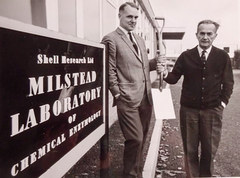 Shell Research Milstead Laboratory of Chemical Enzymology Két férfi áll a Shell Research Ltd Milstead Laboratory of Chemical Enzymology előtt, egyikük ásót tart.