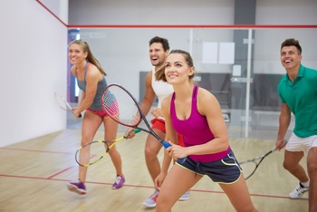 Squash játékosok beltéri pályán Négy ember squash-t játszik egy beltéri pályán, mindegyikük squash ütőt tart.